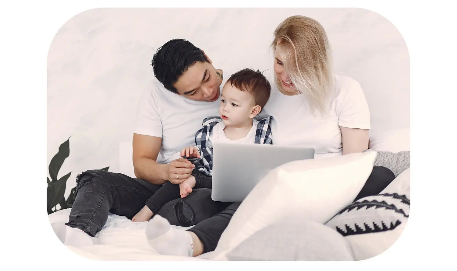 a couple together with a child sitting on a bed with a laptop